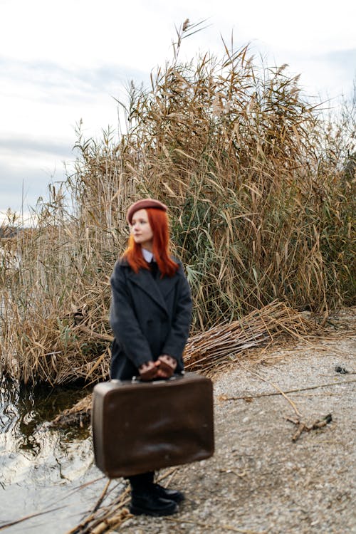 Woman with Suitcase and Rushes on Riverbank