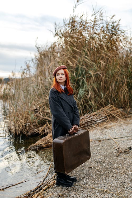 Redhead Woman with Suitcase on Riverbank