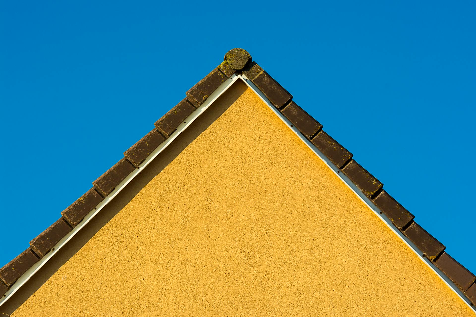 Bright yellow gable wall contrasted by a vivid blue sky, emphasizing minimalist architecture.