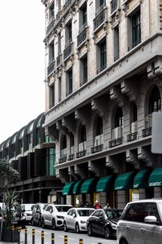 Street scene of a historic building facade with cars parked in a bustling city area.