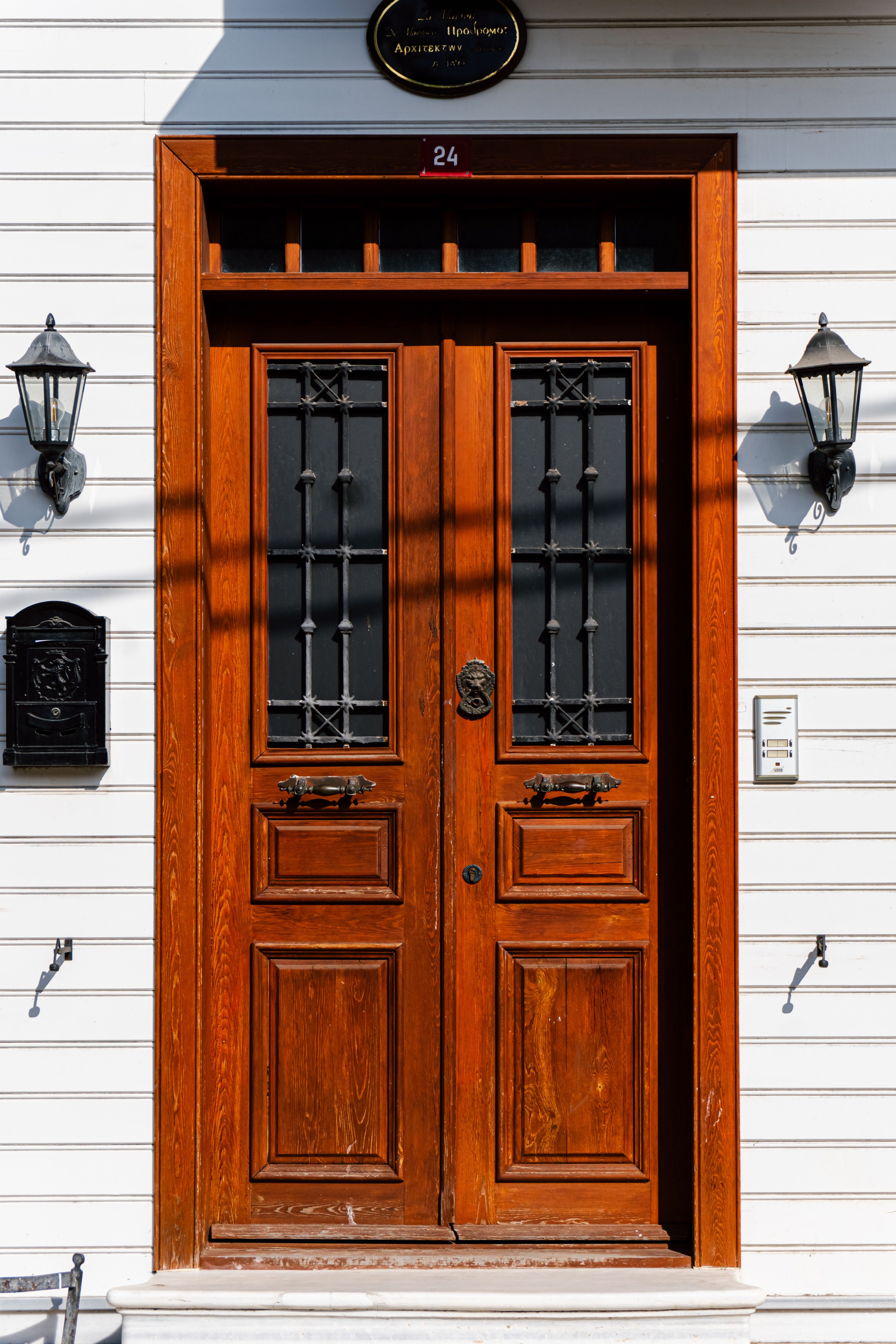 Elegant wooden door with intricate glass panels and flanking wall lights.