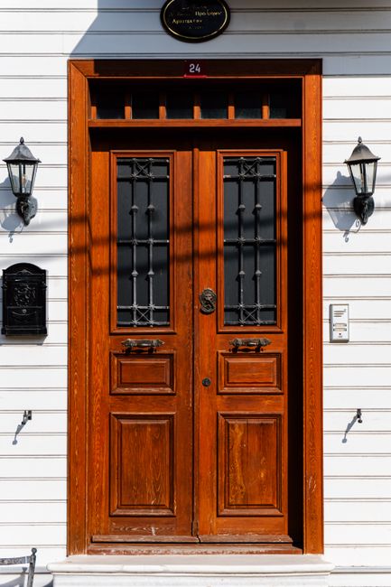 Elegant wooden door with intricate glass panels and flanking wall lights.