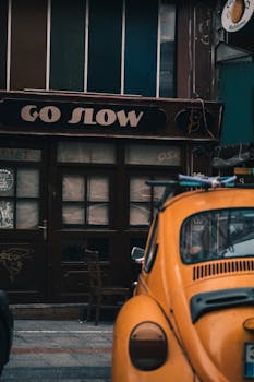 A classic vintage car parked on a city street in front of a shop with a 'Go Slow' sign.