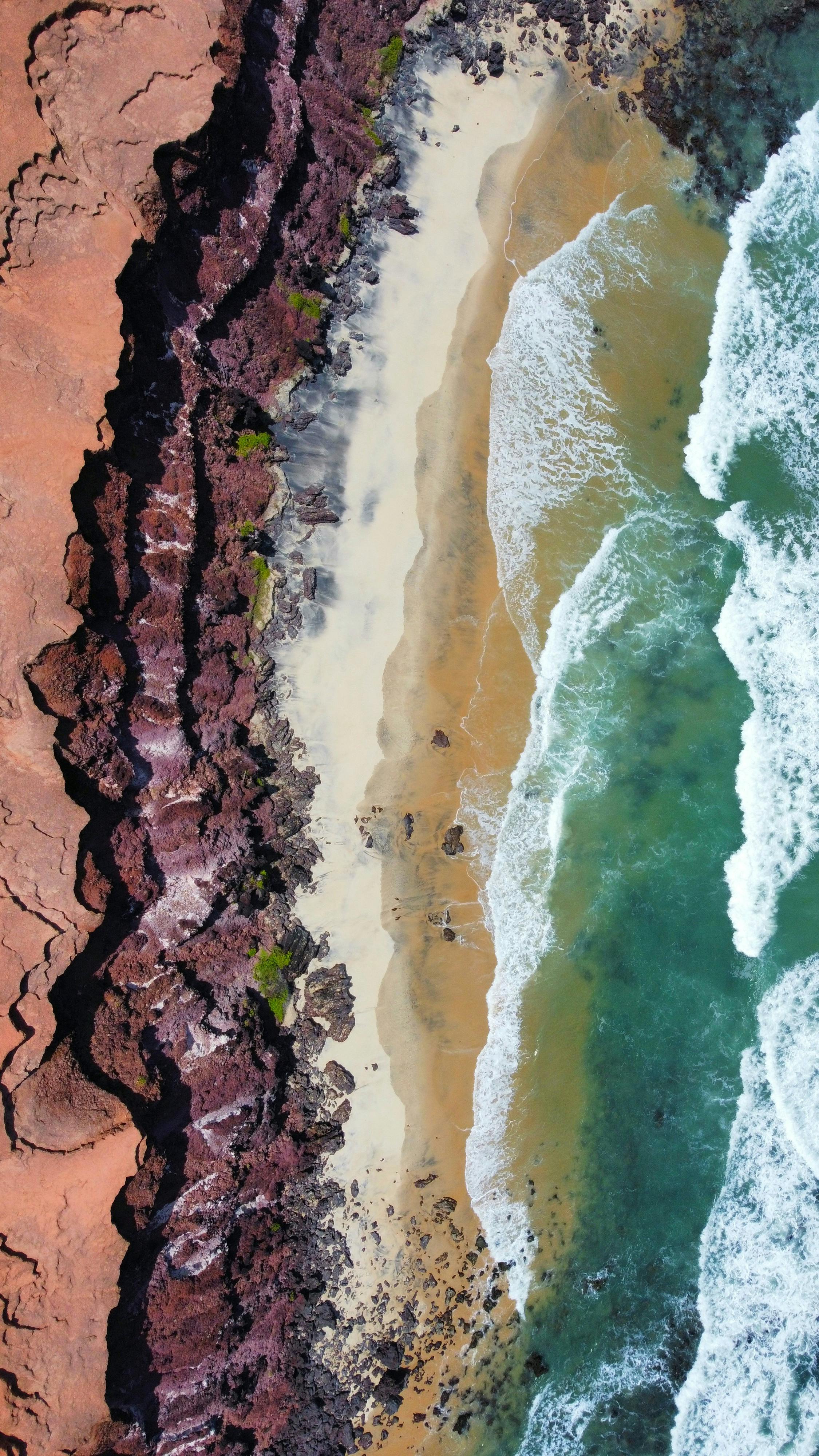 A breathtaking aerial view of a rugged coastline with crashing waves and sandy shore.
