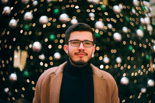 Free Portrait of a young man in a brown coat with Christmas lights and decorations in the background. Stock Photo