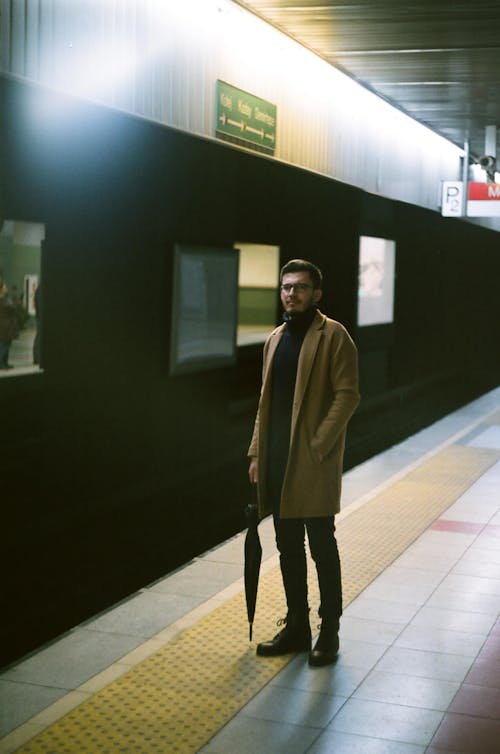 Man in Beige Coat Standing with Umbrella on Platform