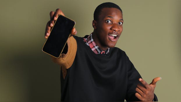 Happy young man showcasing a smartphone while enthusiastically pointing indoors.