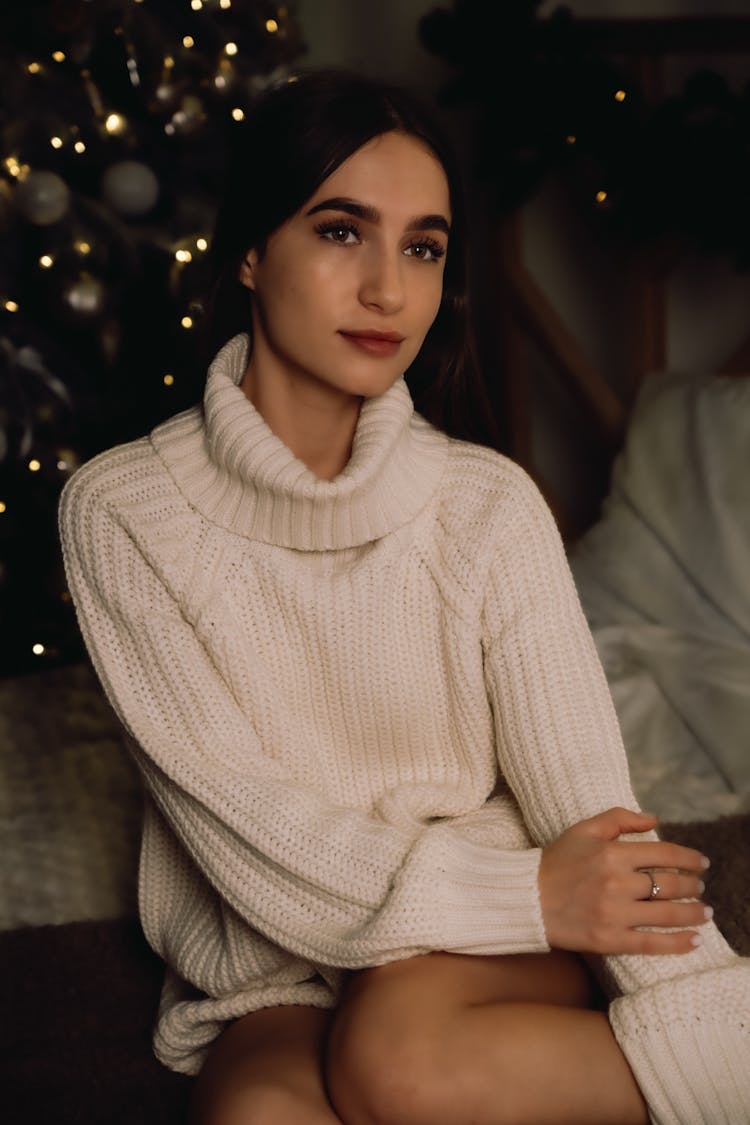 Young Woman In A Sweater Sitting Next To A Christmas Tree