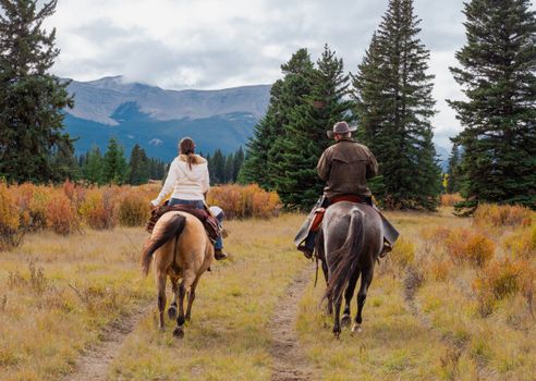 A man and woman horseback riders make their way along a trail in the Ya Ha Tinda Ranch in Alberta, Canada during autumn