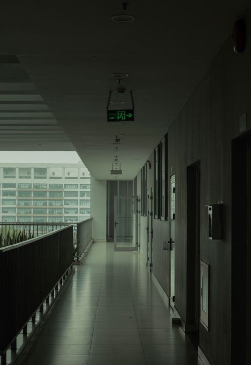 Free A view down a modern residential corridor with emergency exit signage and urban outdoor scenery. Stock Photo