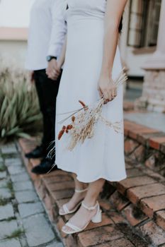 Romantic outdoor wedding scene featuring a bridal bouquet and a couple holding hands.