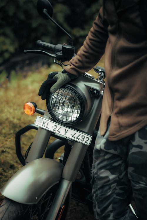 Free A man in camouflage attire standing beside a vintage motorcycle, outdoors in India. Stock Photo