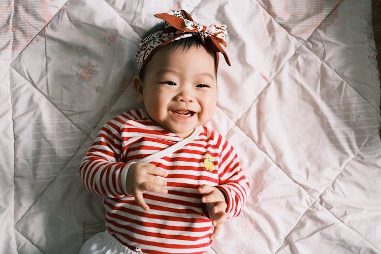 Little Girl Wearing Stripped Shirt Lying On Bed 