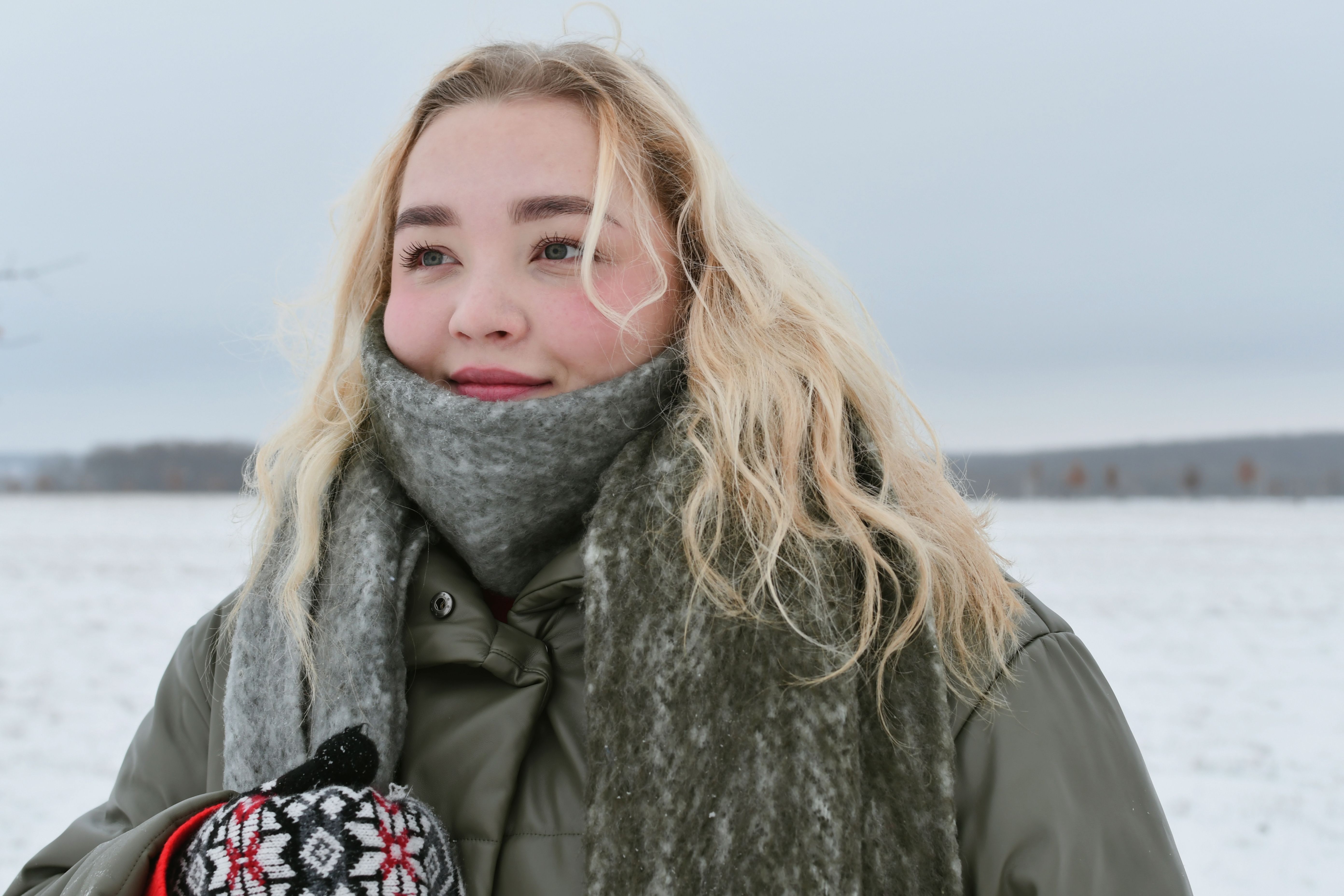 Woman in a snowy field enjoying winter with a scarf and gloves.