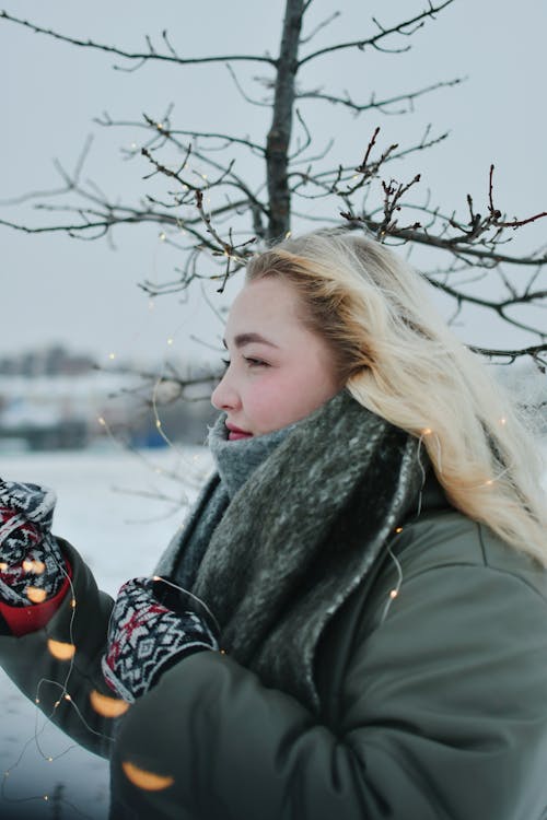 Young Woman in Winter Clothes Entangled in Christmas Lights