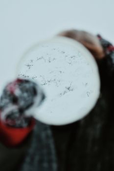 Blurred view of a person holding a circular snowy mirror, creating a mystical winter reflection.