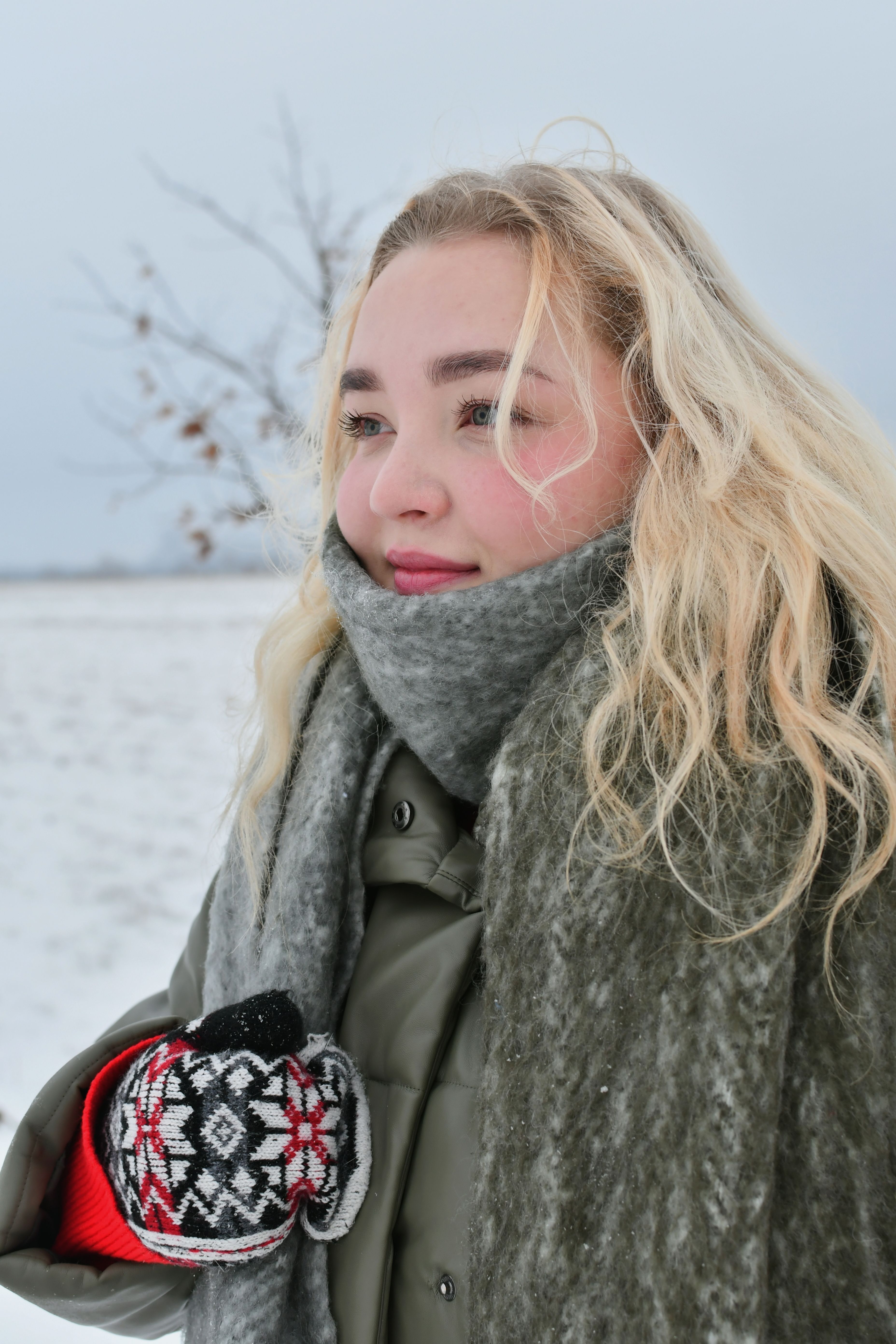 Young woman enjoying a winter day outdoors, wrapped in a wool scarf with snowy fields in the background.