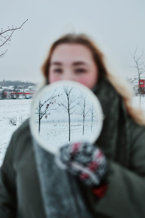 Blonde Woman Holding Mirror with Reflection of Trees in Snow