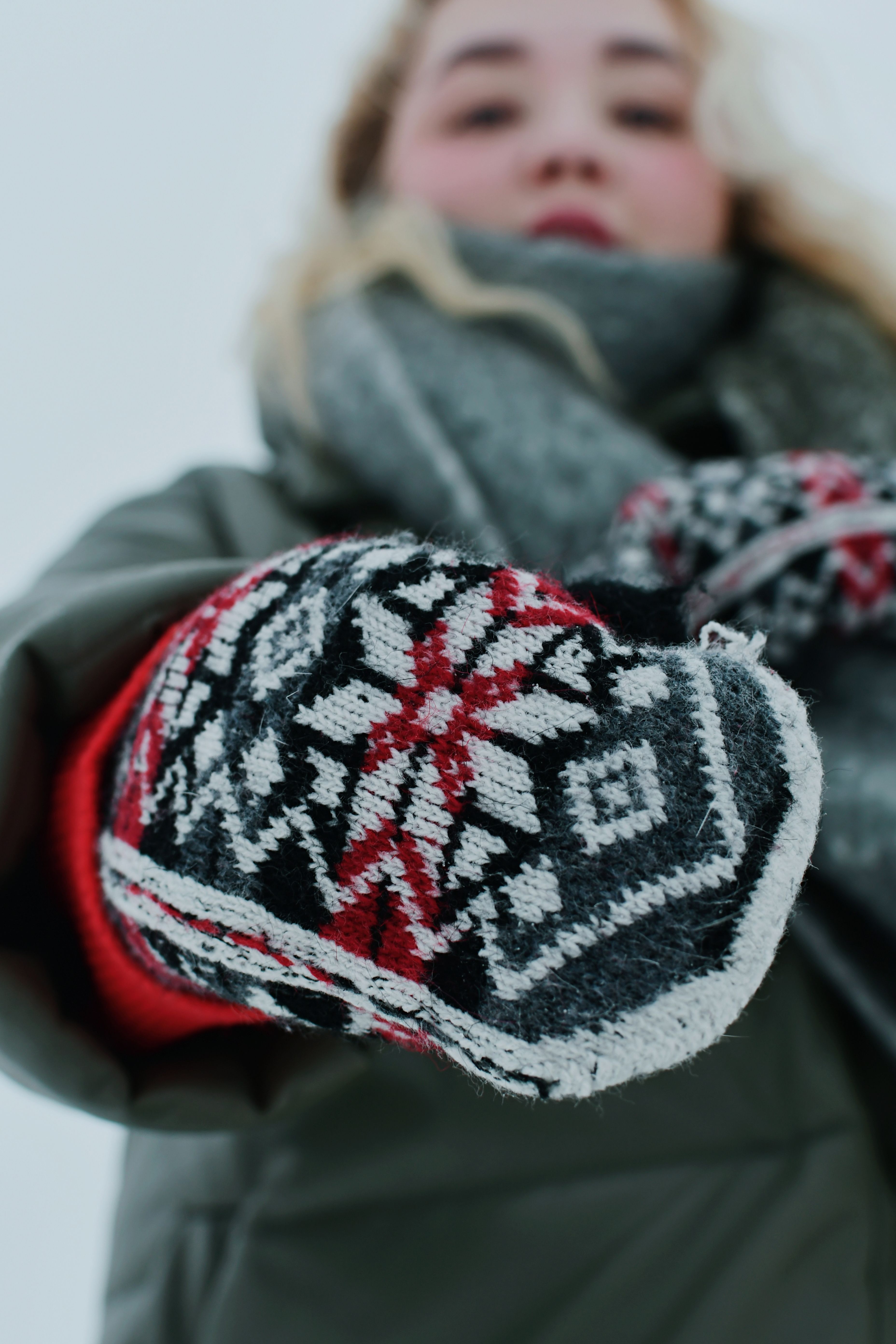 A woman displays cozy knitted mittens outdoors on a winter day.