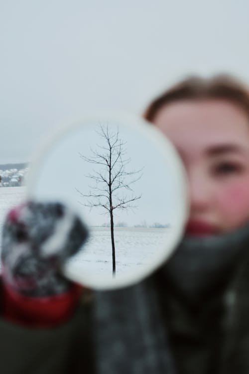 Woman Holding Mirror with Reflection of Tree in Snow