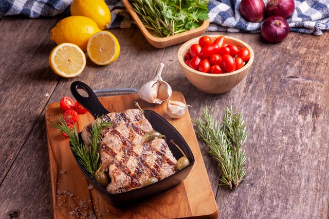 Delicious grilled meat served with fresh herbs, tomatoes, and lemons on a rustic wooden table.