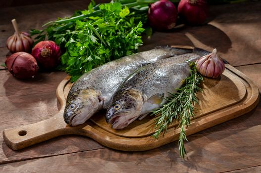 Two fresh raw fish with garlic, rosemary, and onions on wooden board.