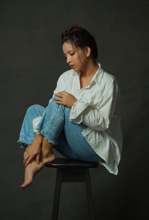 Young Woman in White Shirt and Jeans Sitting on Stool
