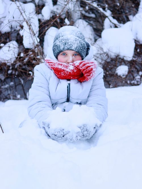 Free A child enjoying winter by playing in the snow, wearing warm clothing and a red scarf. Stock Photo