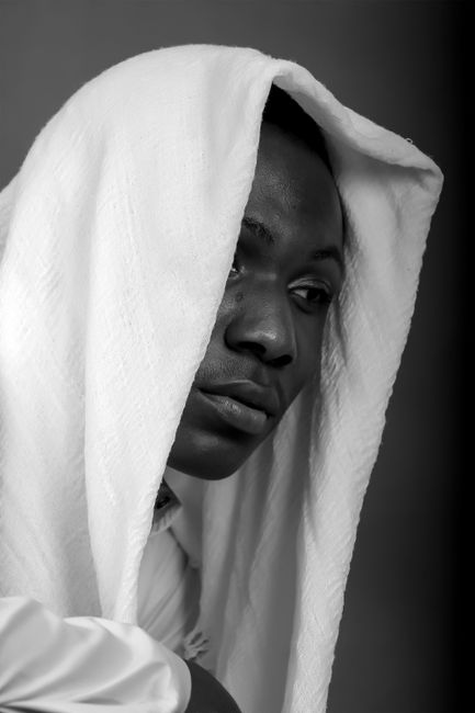 Artistic black and white portrait of a contemplative man with a towel over his head.