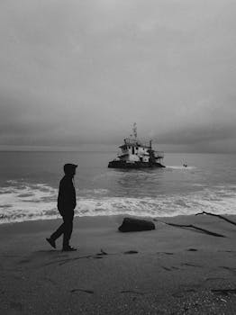 Silhouette of a man walking on a gloomy Chukai beach as a boat drifts in the sea.