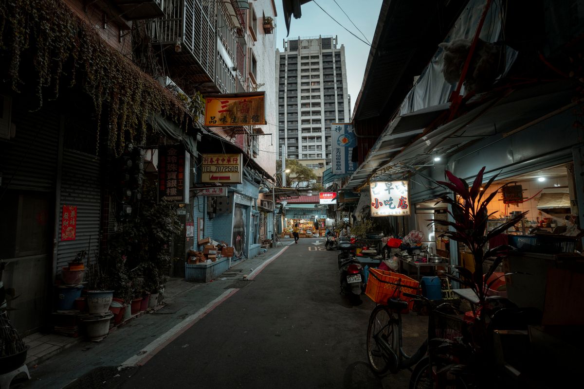 A quiet Taipei alley at dusk, market stalls just lighting up for the night ahead.