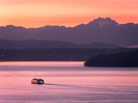 Scenic view of a ferry crossing under a pink sunset sky with mountains in the background in Seattle.