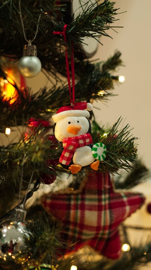Free Charming penguin ornament hanging on a beautifully decorated Christmas tree, creating a festive holiday atmosphere. Stock Photo