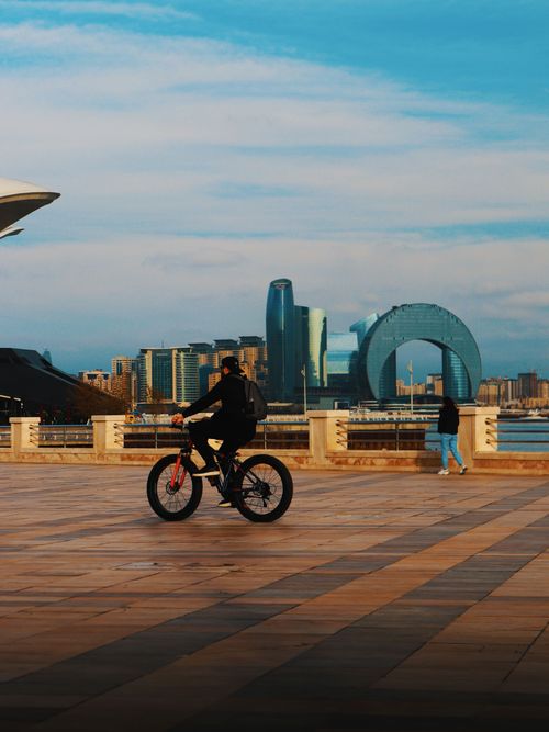 Free A man rides a bicycle along the waterfront with Baku's modern skyline in the background. Stock Photo