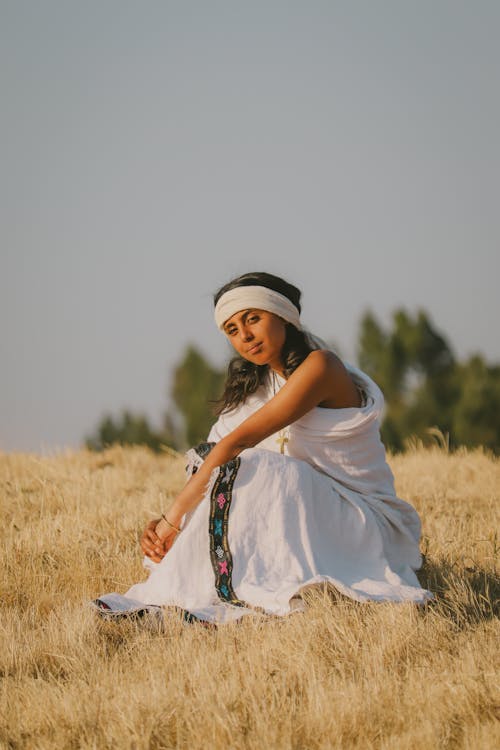 Young Woman in a White Dress and a Headband Sitting in a Field
