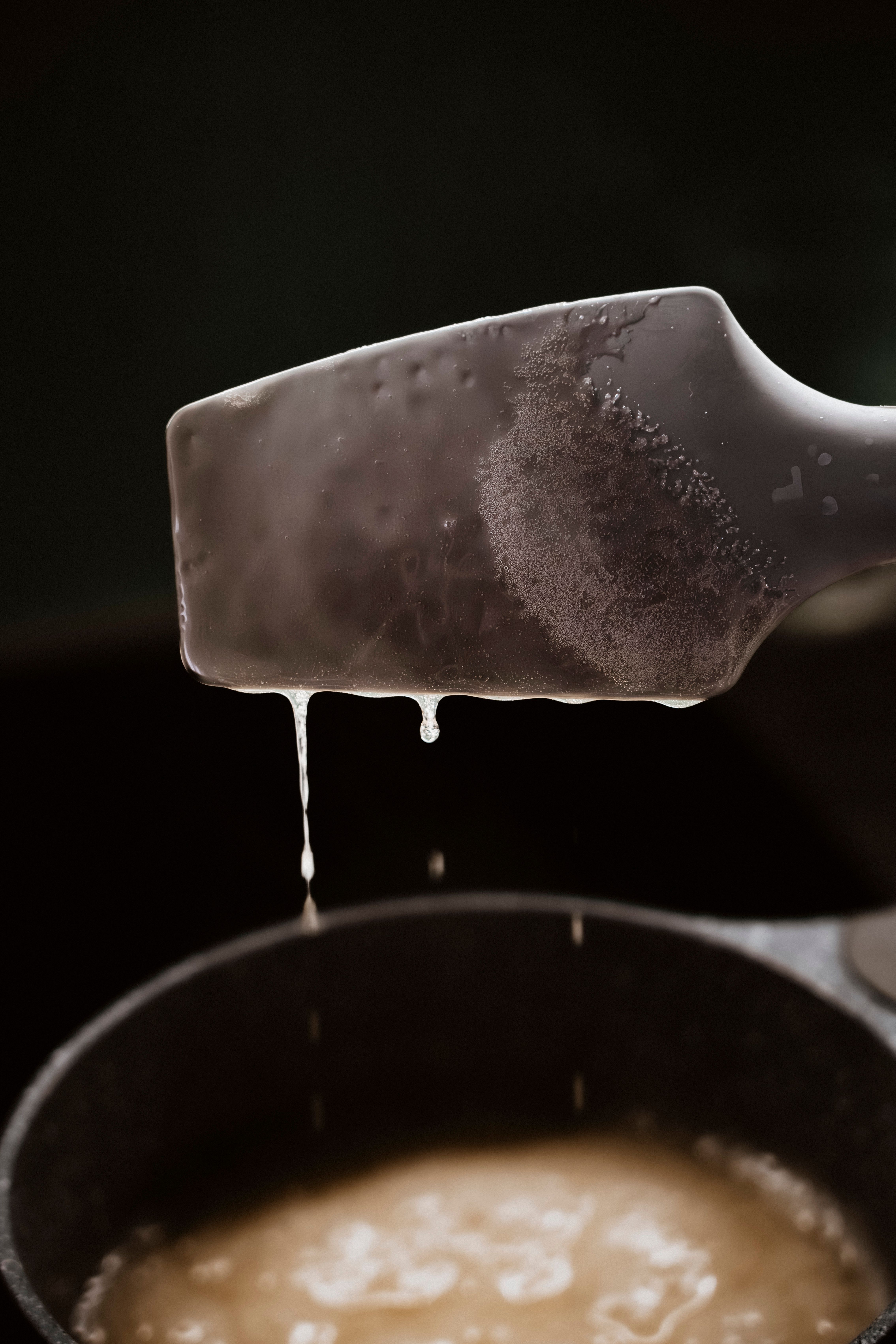 Cooking grease dripping from a spatula above a pan