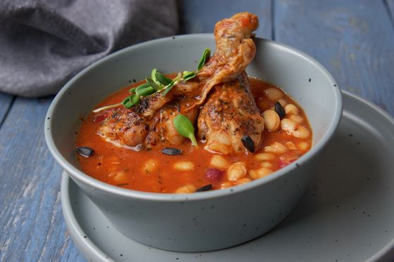 Browned herb-crusted chicken drumsticks in tomato white bean stew with microgreens and pumpkin seeds