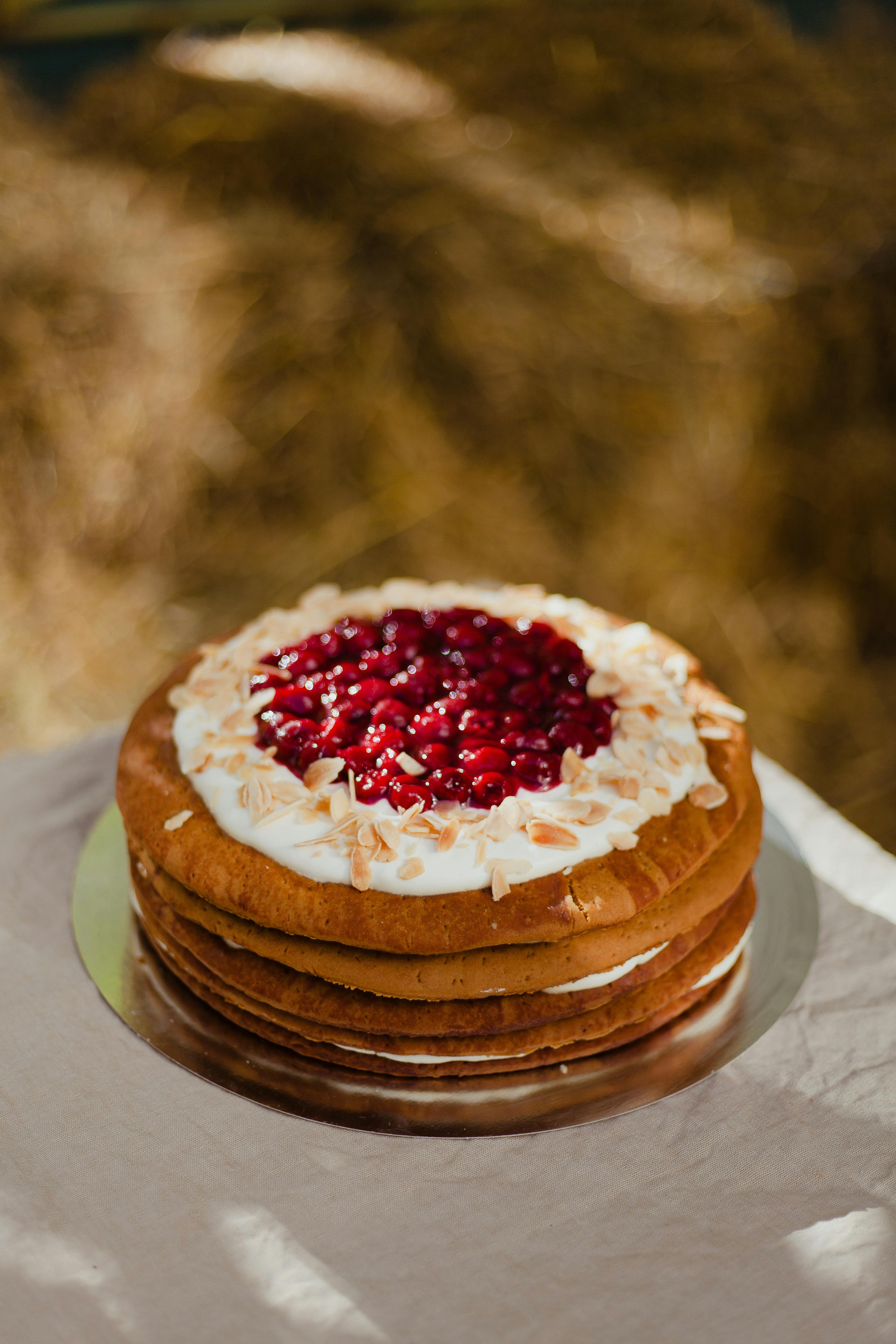 Delicious rustic layer cake topped with cream and pomegranate seeds on a table.