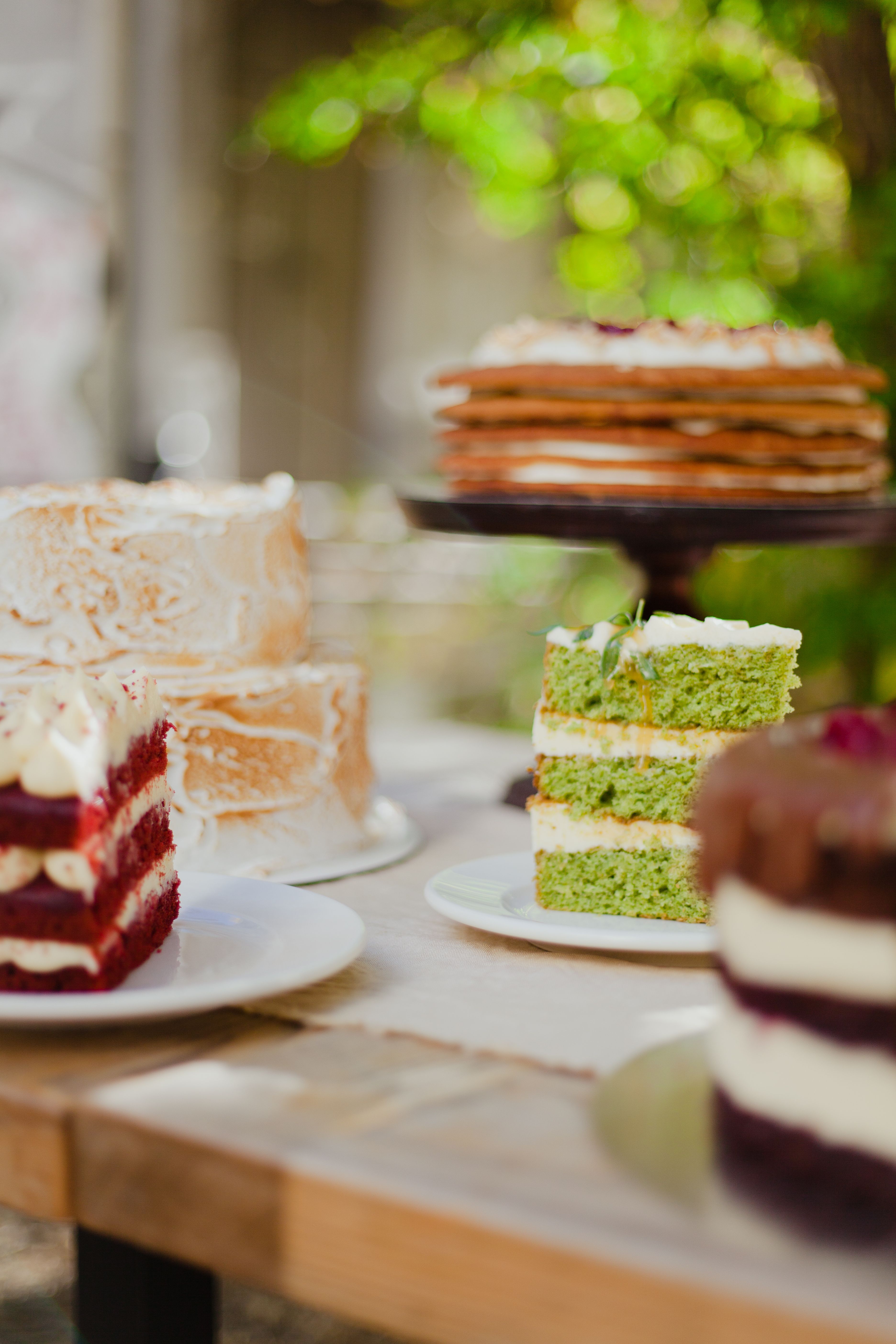 A selection of layered cakes on a rustic table outdoors, perfect for dessert photography.