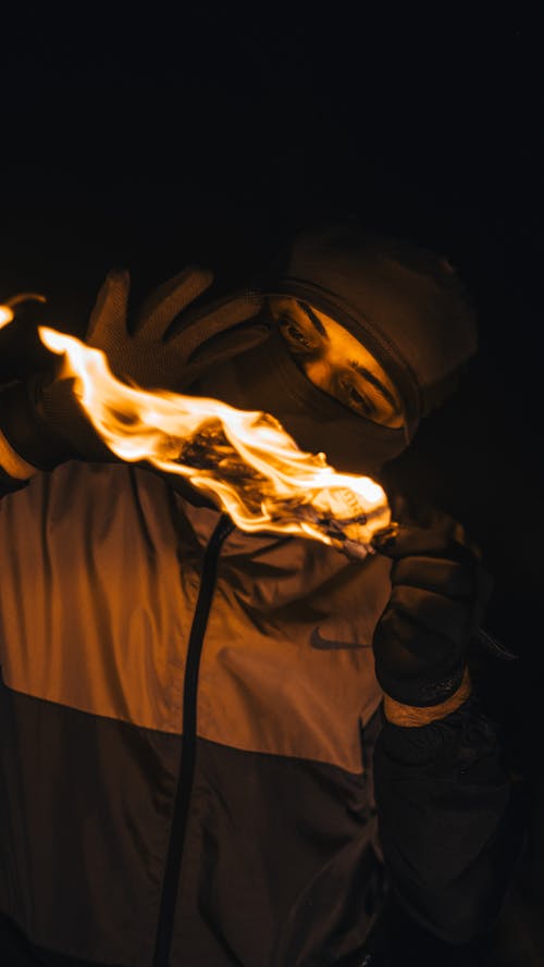 Man in Balaclava Holding Burning Item at Night