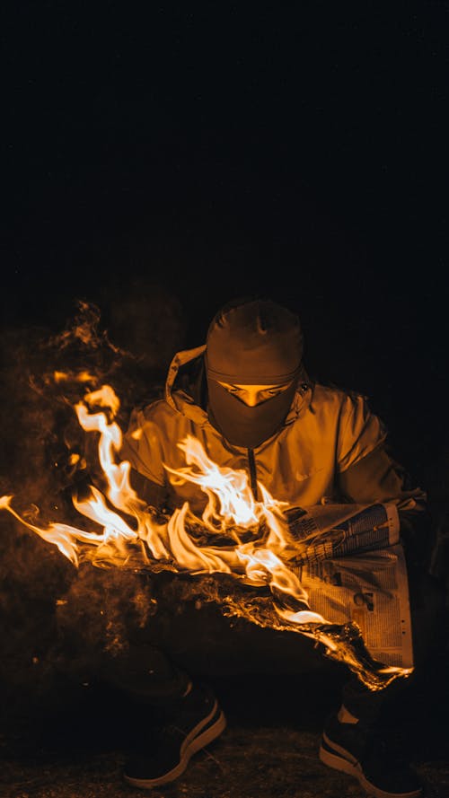 Man in Balaclava with Newspaper on Fire at Night