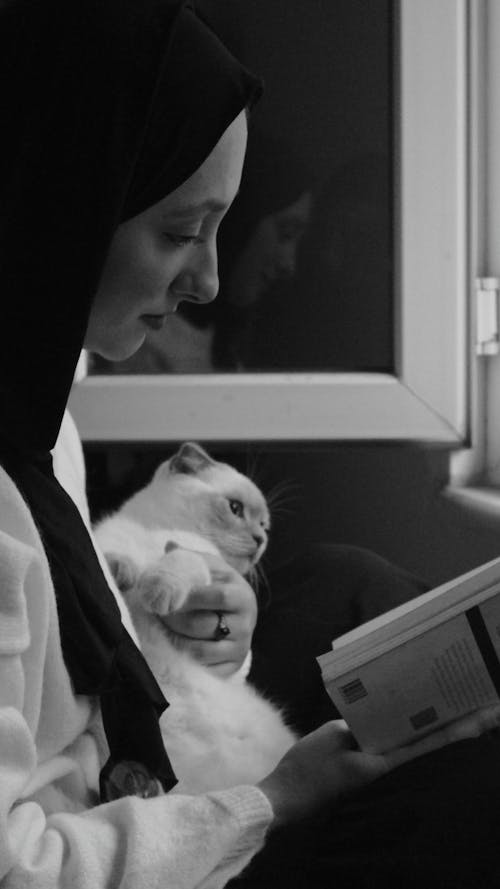 Woman in Hijab Holding Cat and Reading Book