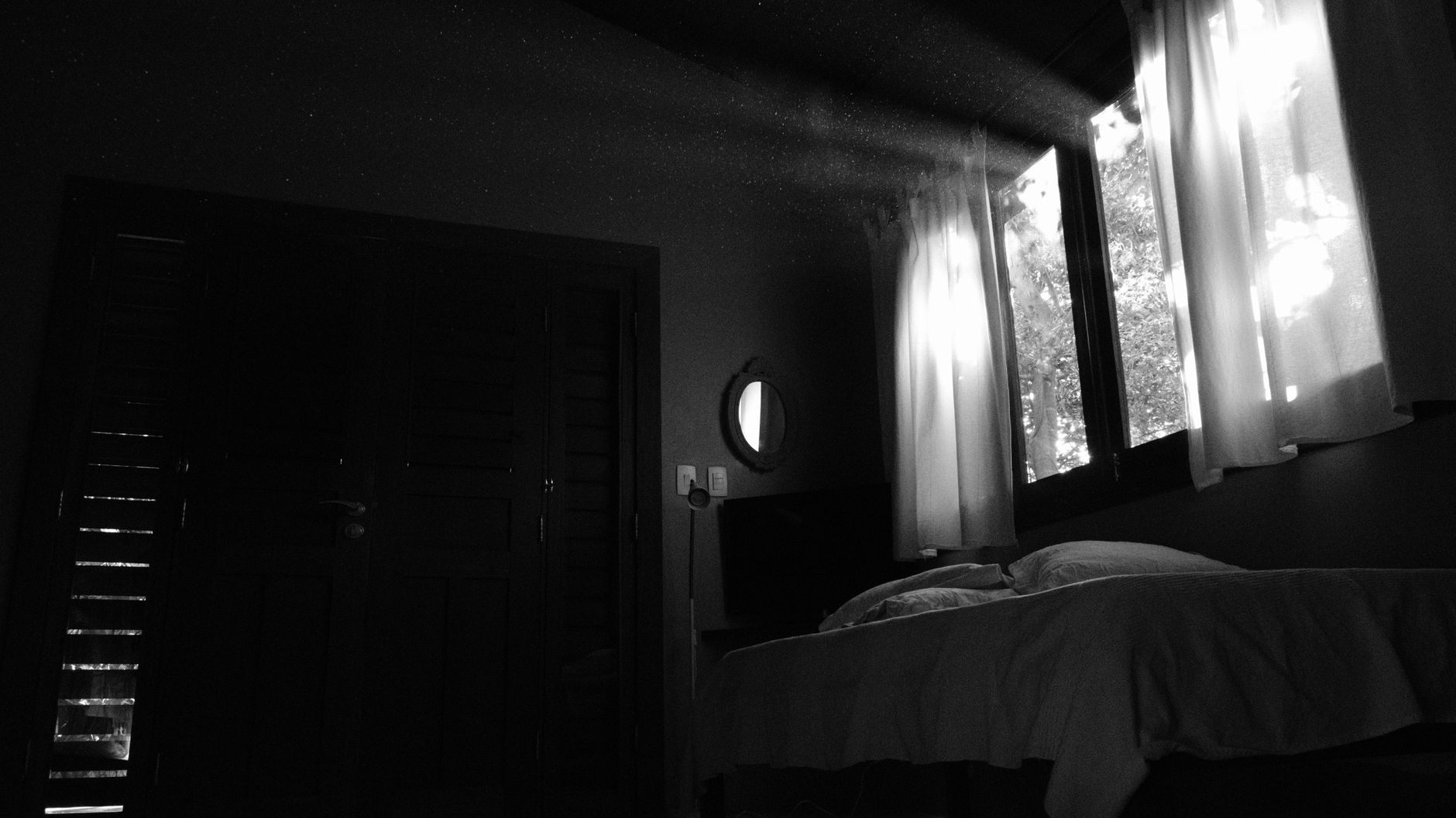 Black and white photo of a bedroom with sunlight streaming through window curtains. Perfect for interior design inspiration.