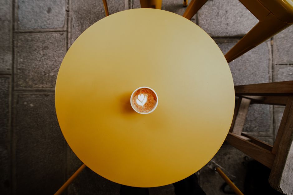 Overhead view of coffee cup with latte art on a round yellow table in a Parisian cafe.