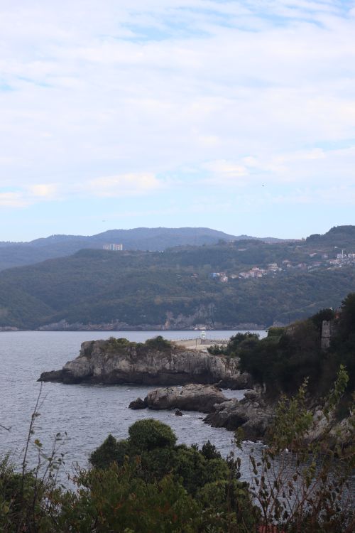 Free A serene view of a rocky shoreline with distant hills under a sky filled with clouds. Stock Photo