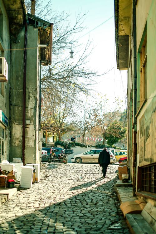 Free A picturesque cobblestone alley in a European town during a sunny day with a pedestrian. Stock Photo
