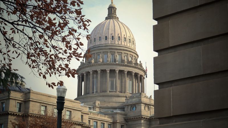 A view of the Idaho State Capitol Building framed by autumn leaves.