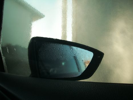 Car side mirror reflecting wet, foggy view with raindrops