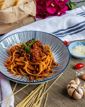 Plate of spaghetti bolognese topped with fresh basil, surrounded by garlic, cheese, and bread.