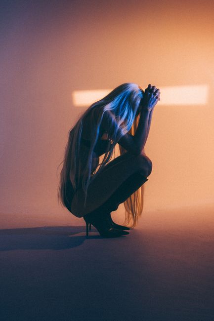 Silhouette of a woman in high heels squatting, set against a warm yellow background.